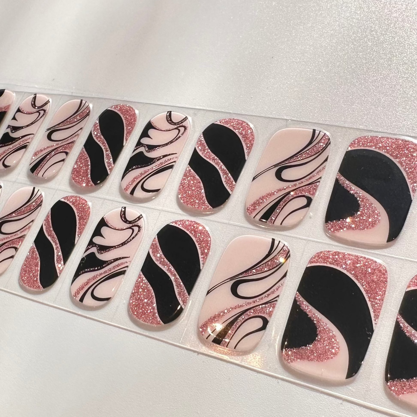 Close-up of pink glitter and black marble effect gel nail wraps with swirl pattern