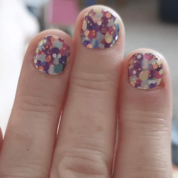 Colourful polka dot nail wraps on three fingers showing purple yellow multicoloured party design