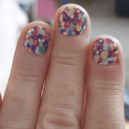 Colourful polka dot nail wraps on three fingers showing purple yellow multicoloured party design