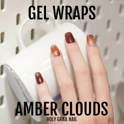 Hand displaying amber clouds gel nail wraps with brown to orange gradient marble effect