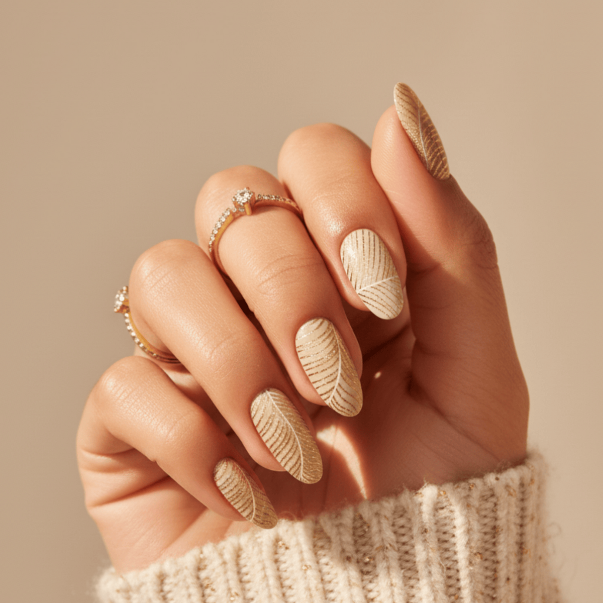 Feather pattern gel nail wraps in nude tones on hand wearing cream jumper