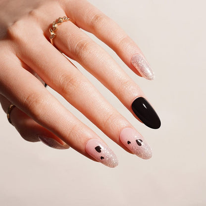 Pink glitter and black gel nail wraps with heart accents on hand