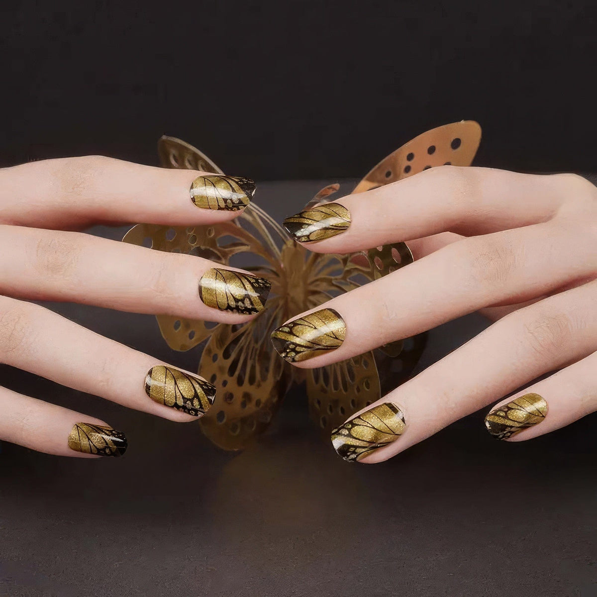 Hands showing golden brown butterfly wing gel nails with intricate wing patterns