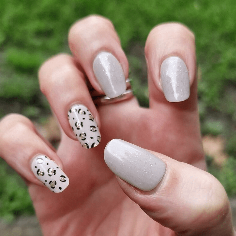 Grey gel nail wraps with black and white cheetah print design on hand outdoors