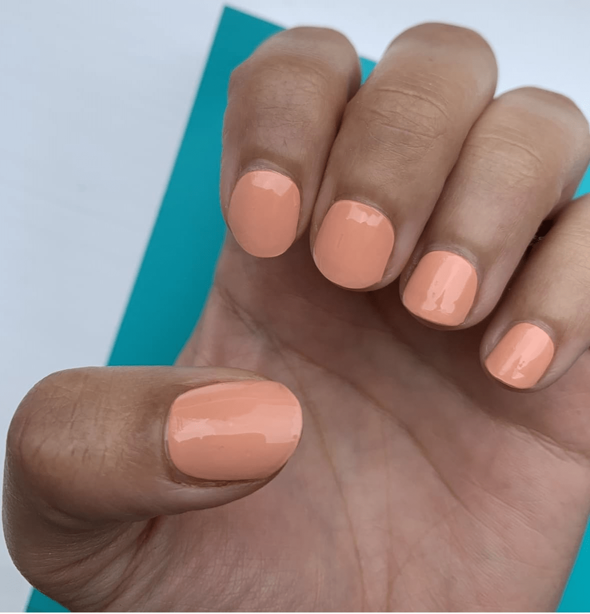 Hand wearing glossy coral orange gel nail wraps showing finished at-home manicure