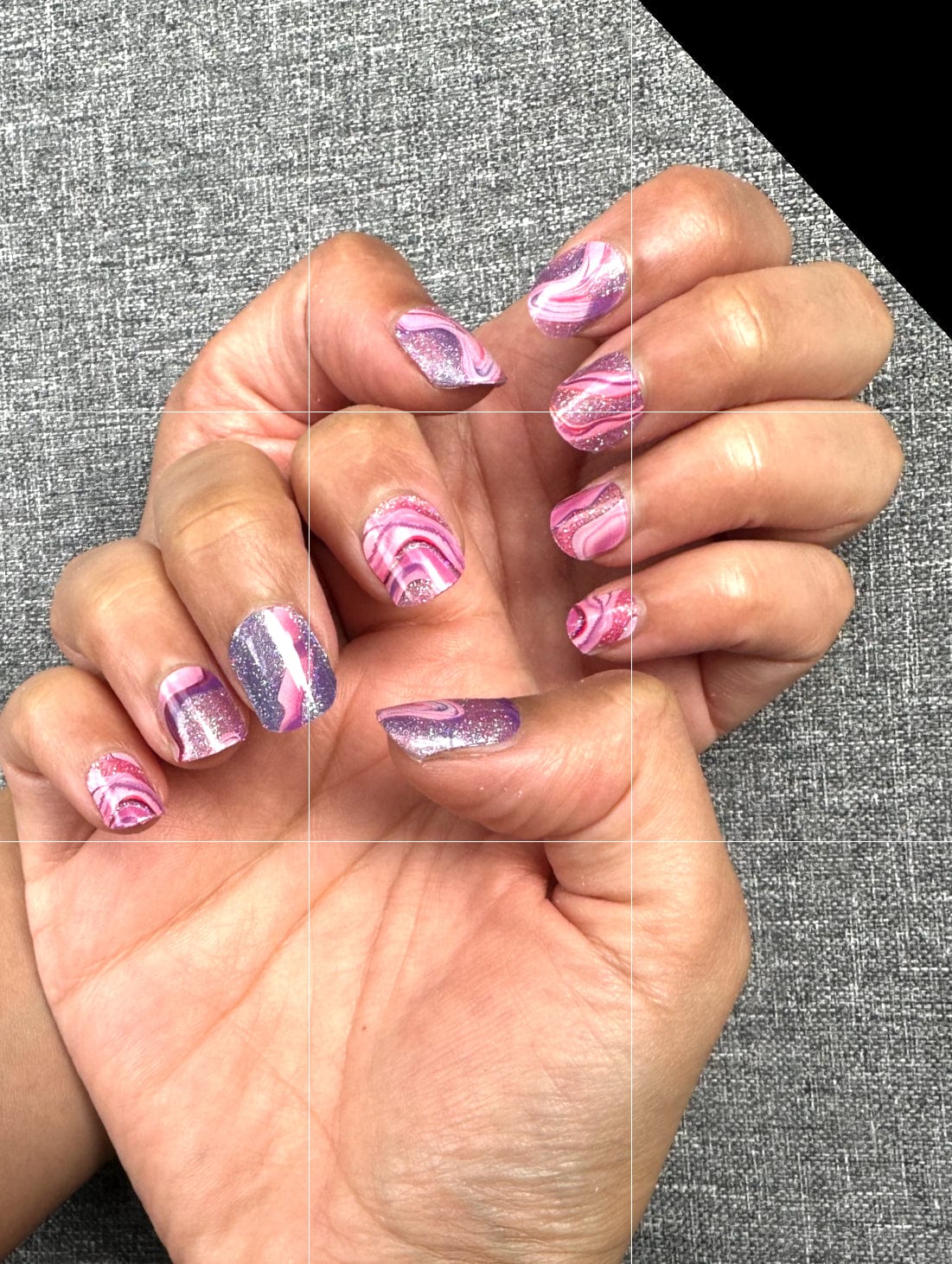 Pink and purple swirl gel nail wraps on hands displaying psychedelic marble patterns