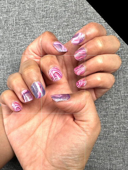 Pink and purple swirl gel nail wraps on hands displaying psychedelic marble patterns