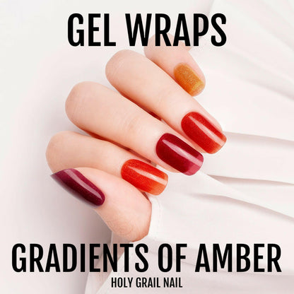 Hand wearing glossy gel nail wraps in amber gradient from burgundy to orange ombre design