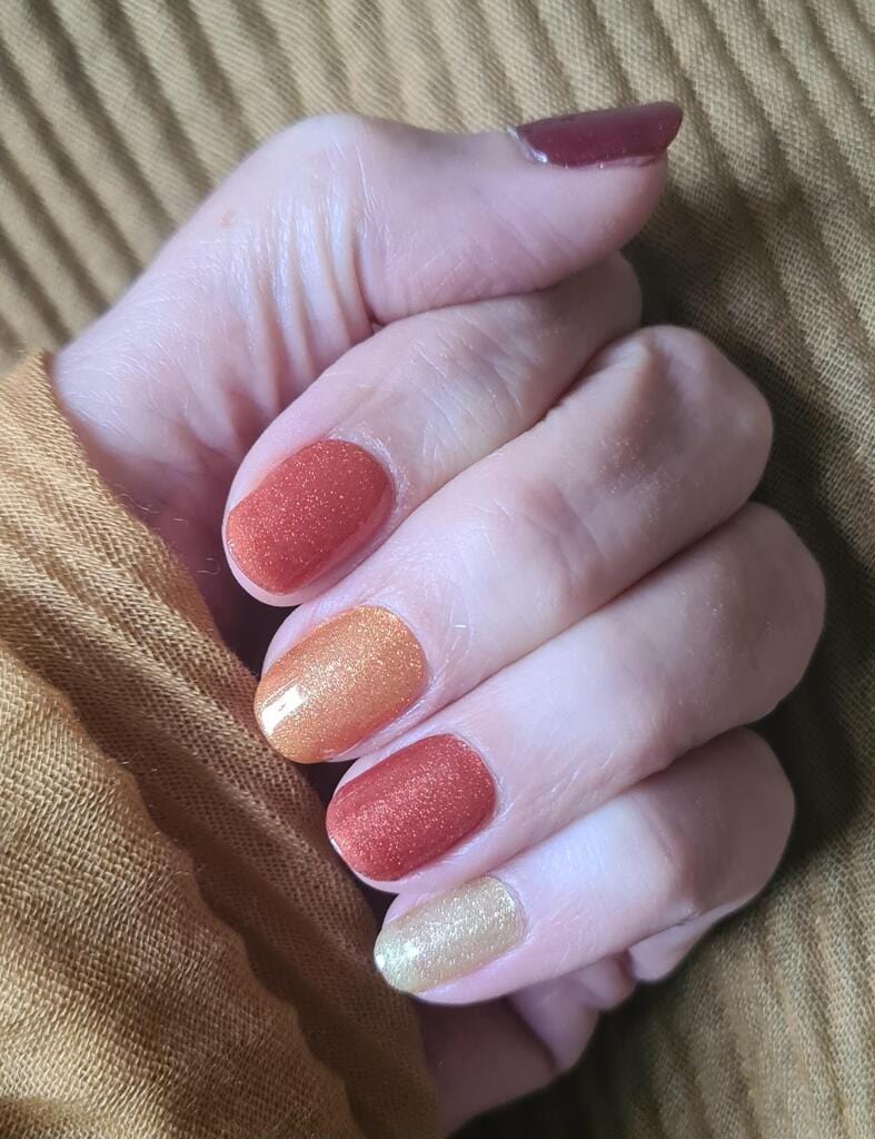 Close-up of gel nail wraps in warm amber gradient tones from coral to golden orange