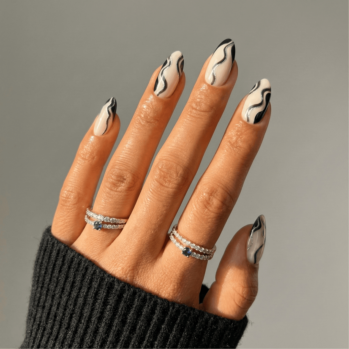 Black and white smoke wave gel nail wraps on hand with silver rings