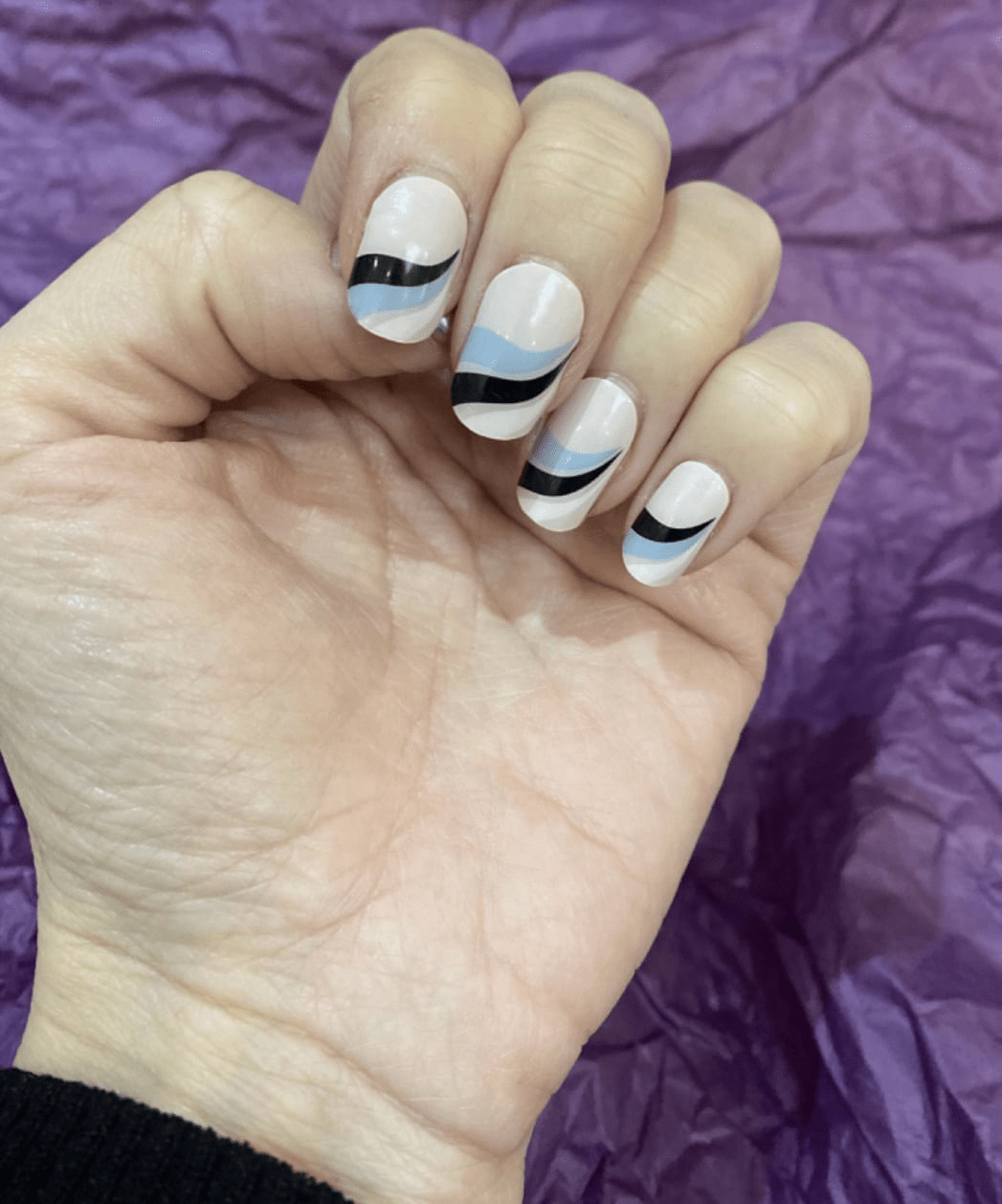 Abstract wave design gel nail wraps in white and black with blue accents on hand