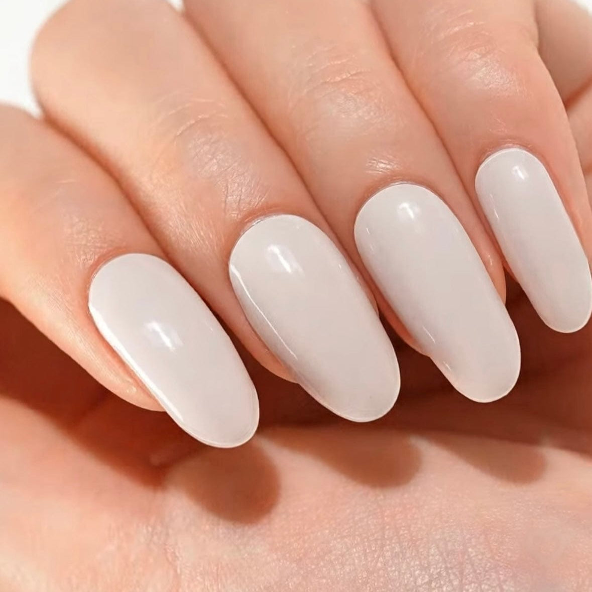 Glossy white oval gel nails on hand showing classic bridal nail art finish