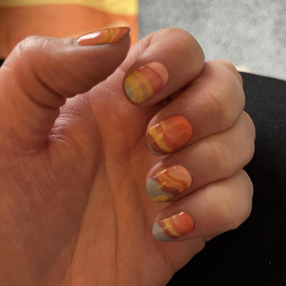 Hand displaying orange gradient gel nail art with marble flowing pattern