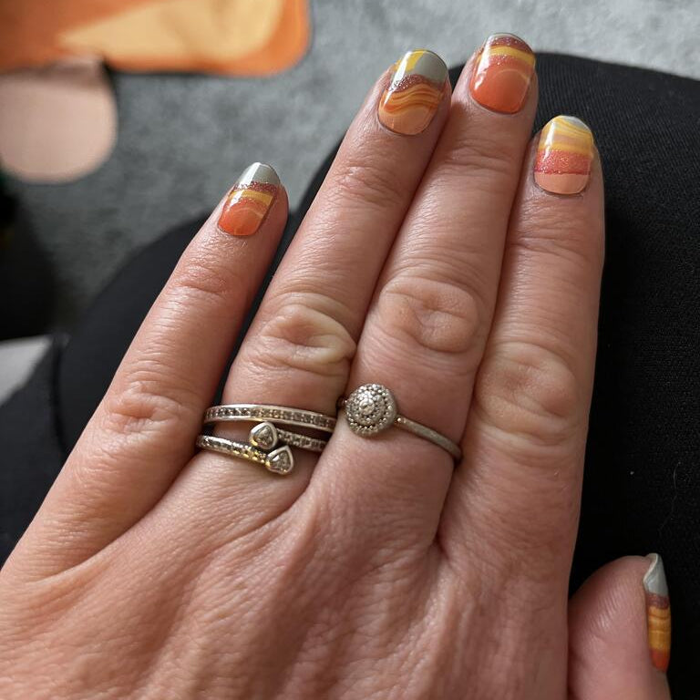 Manicured hand with orange marble gel nail wraps showing flowing lava design