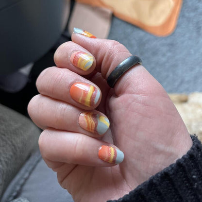 Hand wearing orange marble gel nail wraps with flowing terracotta gradient design