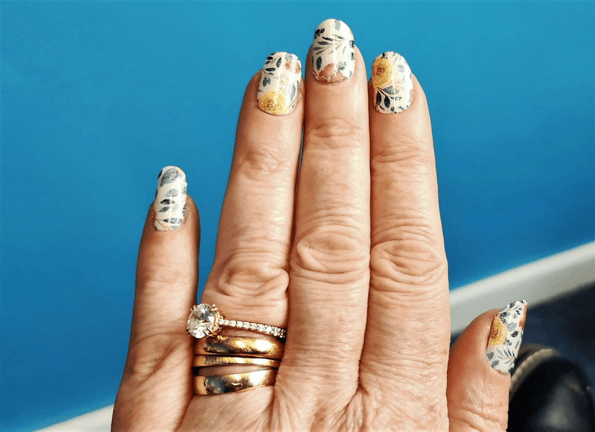 Hand wearing floral gel nail wraps with vintage botanical design in pastel colours