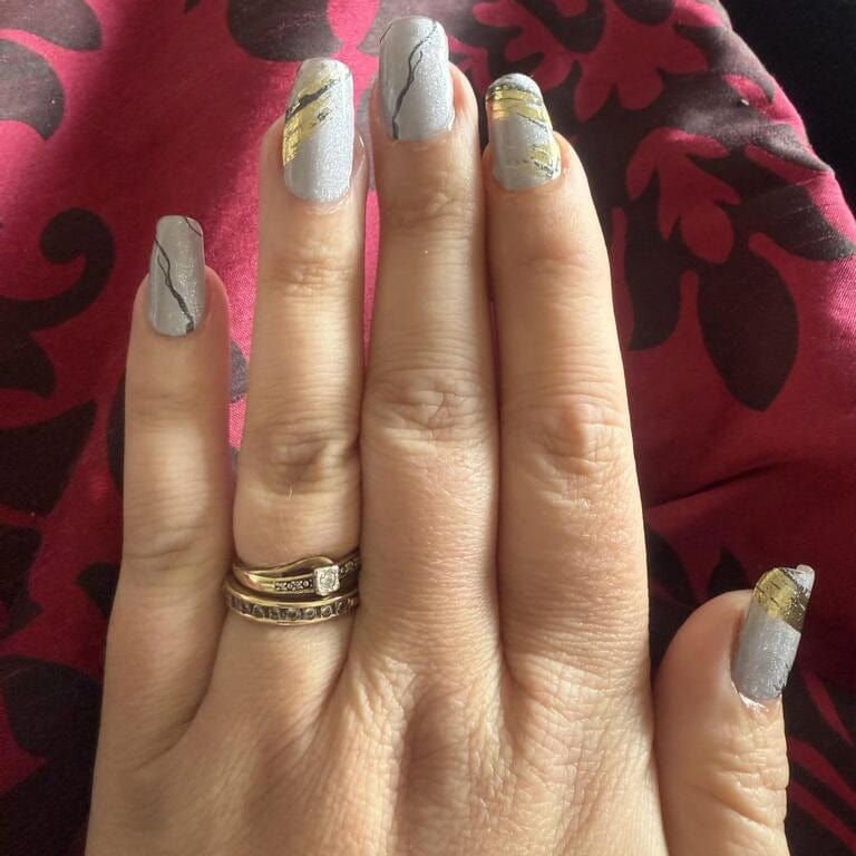 Grey marble gel nail wraps with gold accents applied on hand manicure