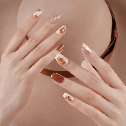 Brown and nude gel nail wraps with crystal patterns applied on manicured hands