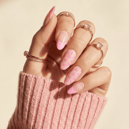 Pink heart pattern gel nail wraps on hand with gold rings
