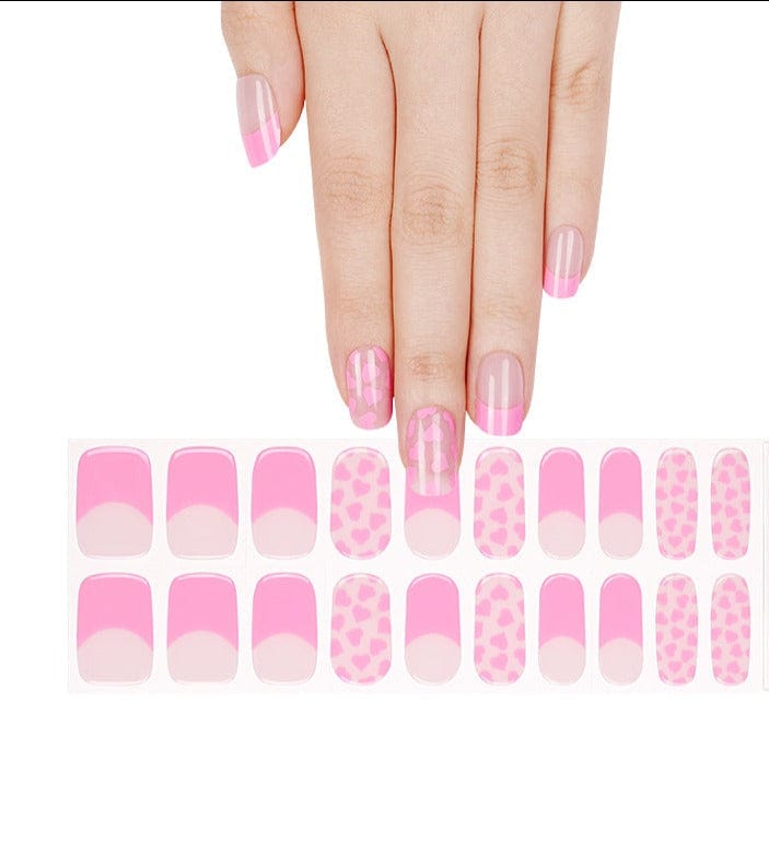 Hand wearing pink gel nail wraps with heart patterns and French tips