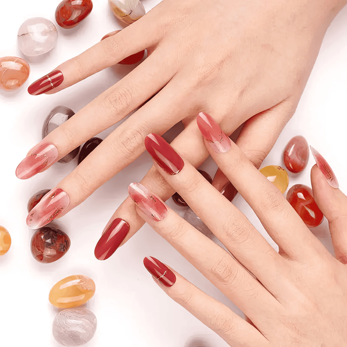 Hands displaying red burgundy chrome gel nail wraps with gold chain detailing surrounded by gemstones