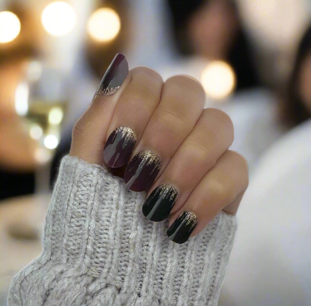 Hand wearing burgundy and green gel nail wraps with metallic gold glitter accents
