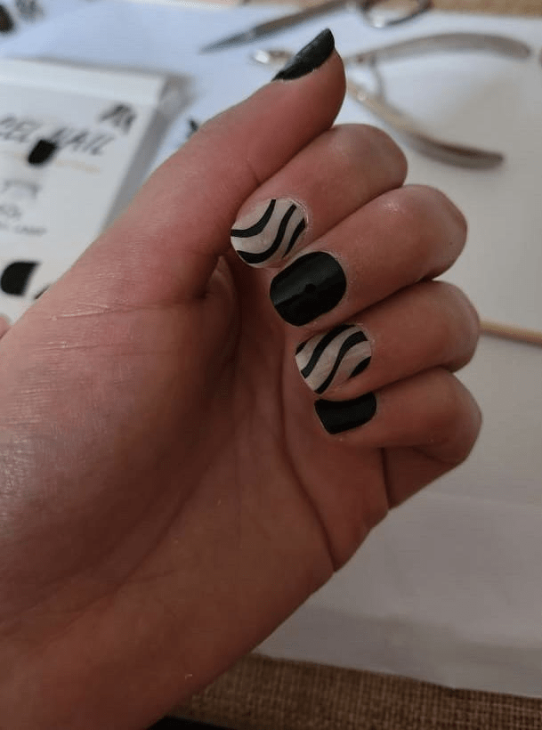 Hand wearing black and white striped gel nail wraps with zebra pattern design