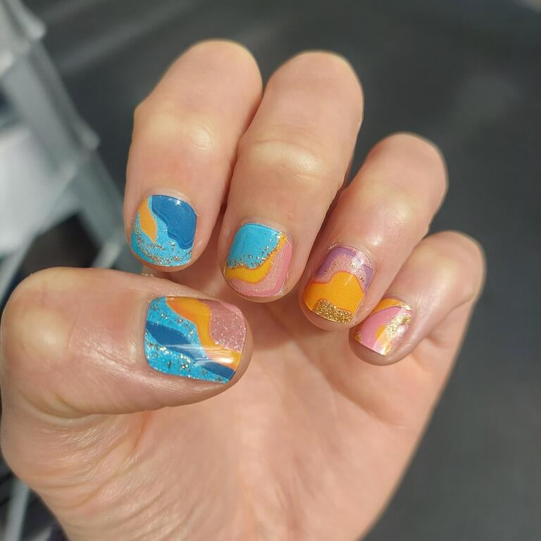 Abstract gel nail wraps on hand featuring blue orange pink marble effect with glitter