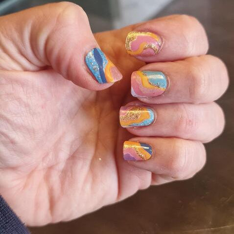 Hand wearing abstract gel nail wraps in blue orange pink with gold glitter details