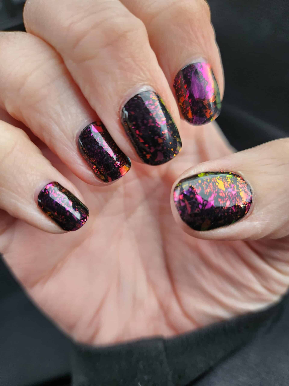 Dark holographic gel nails on hand showing rainbow glitter and metallic finish