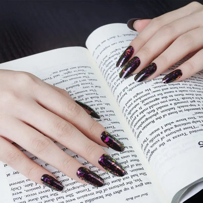Hands with dark sparkly gel nail wraps holding open book showing gothic nail art