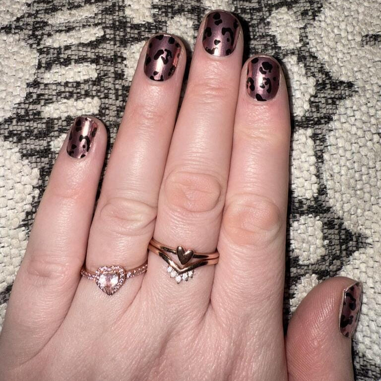 Hand displaying pink chrome leopard print gel nails with black animal print