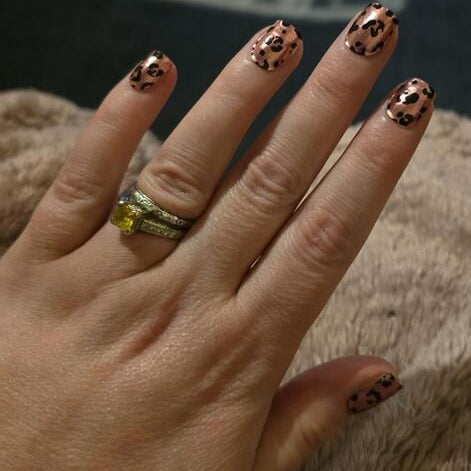 Hand wearing pink leopard print gel nails with black spots animal print