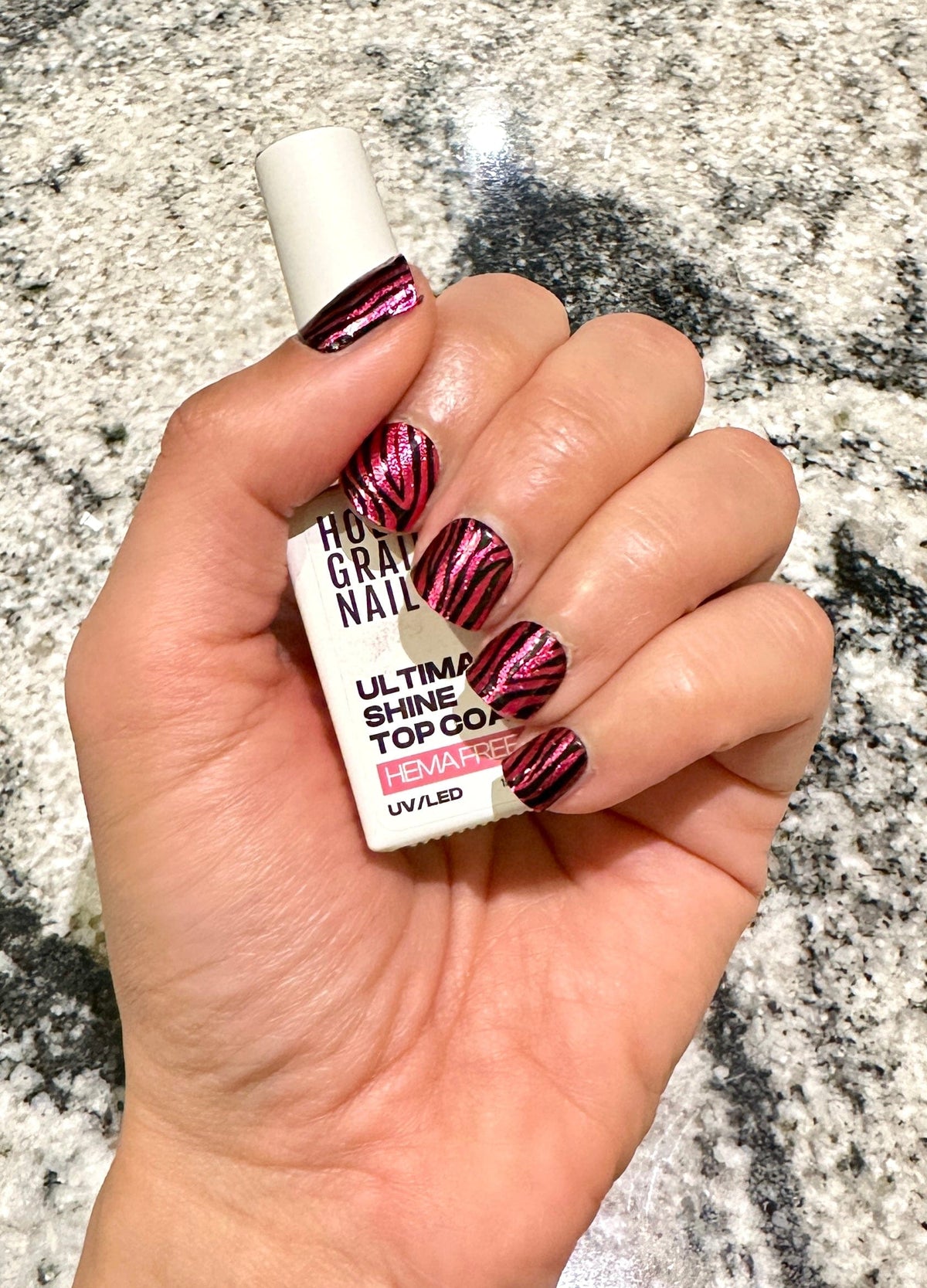 Hand holding topcoat bottle showing burgundy zebra gel nail wraps manicure