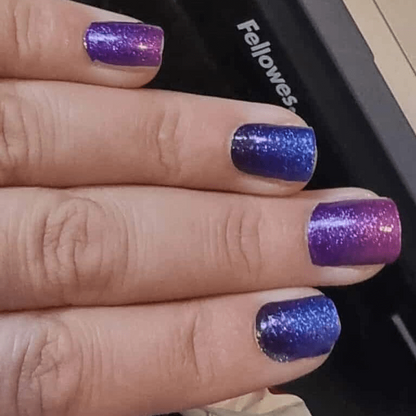 Purple blue glitter gradient nail wraps on hand displaying sparkly ombre manicure finish