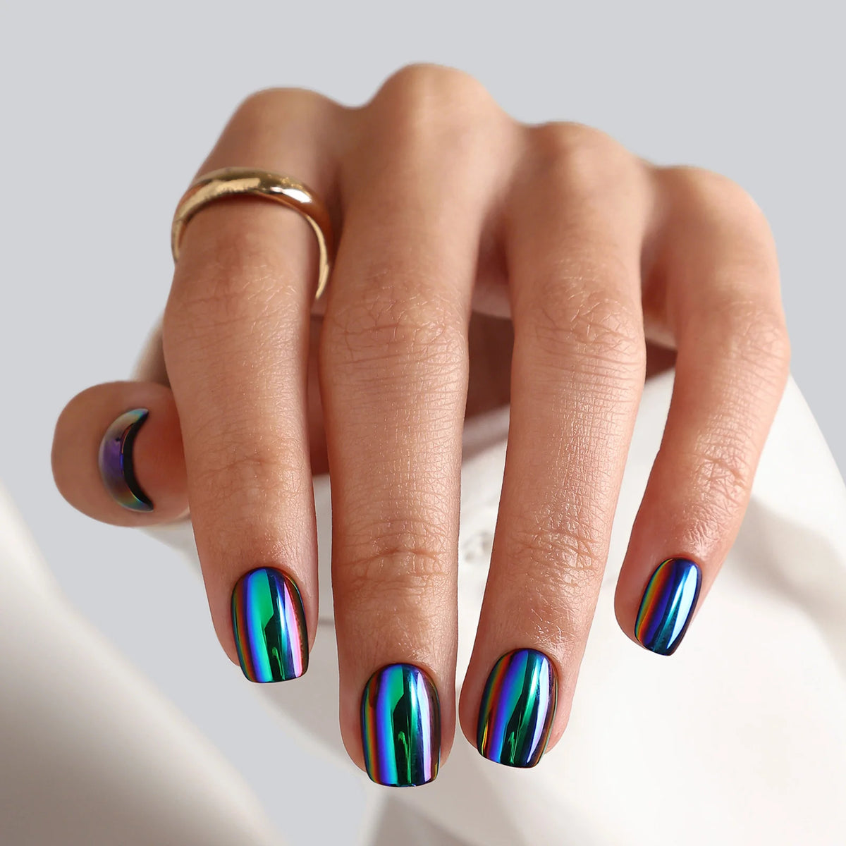 Short square press-on nails with oil-slick chrome finish in iridescent blue, green and purple.